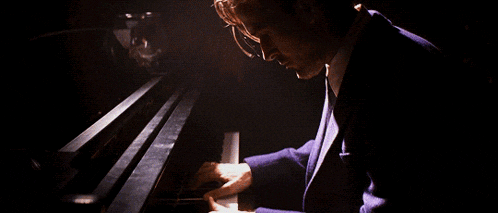 a man in a suit plays a piano in a dark room