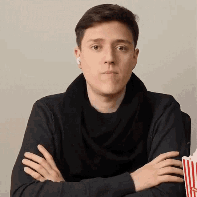 a man is sitting at a table with his arms crossed and holding a popcorn bucket .