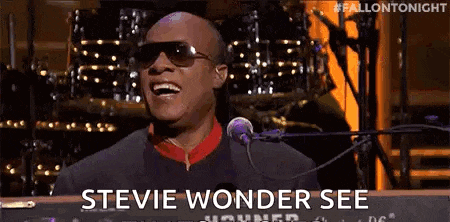 stevie wonder is singing into a microphone while playing a keyboard on a stage .