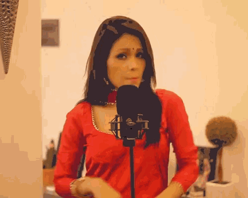 a woman in a red top is singing into a black microphone