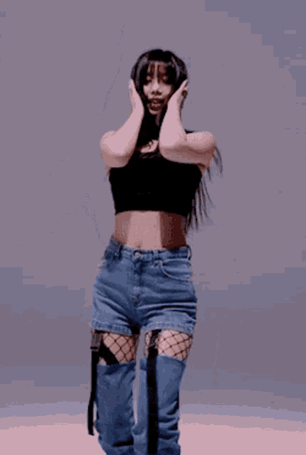 a woman in a black crop top and blue jeans is covering her ears while dancing .