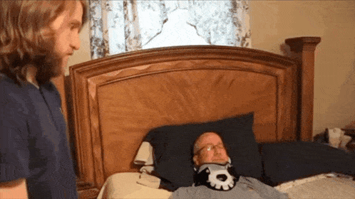 a man standing next to a man laying on a bed with a neck brace