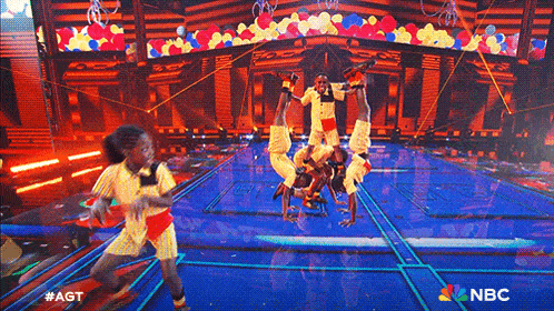 a group of children are doing a handstand on a stage in front of balloons .
