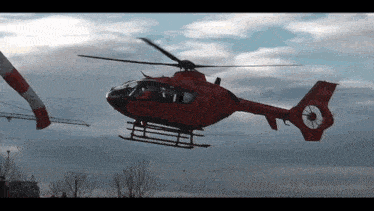 a red helicopter is flying in the sky with a white and red tail