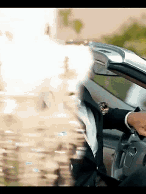 a man in a suit is driving a car and adjusting his watch