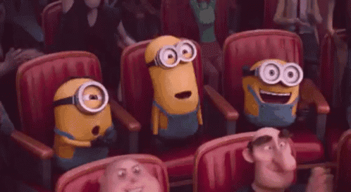 a group of minions are sitting in a row of red chairs in a theater .