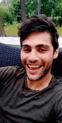 a man with a beard is sitting on a couch smiling .