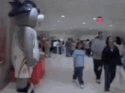a blurred image of a group of people walking in a hallway with a mascot in the background .