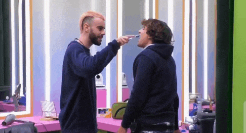 a man is brushing another man 's teeth in a room .