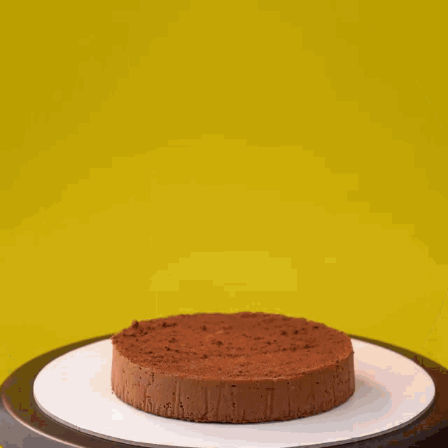 a chocolate cake is being decorated with frosting on a yellow background