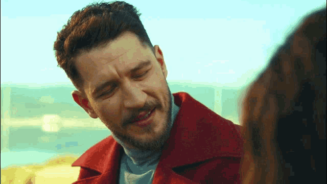 a man with a beard wearing a red coat is looking at a woman