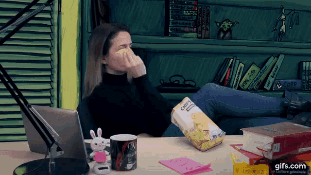 a woman sits at a desk with a bag of chips