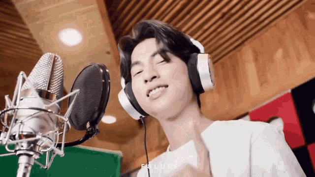 a young man wearing headphones is singing into a microphone in a recording studio .