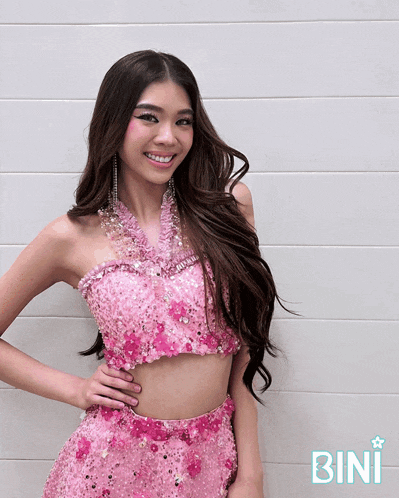 a woman in a pink dress is smiling in front of a wall that says bini