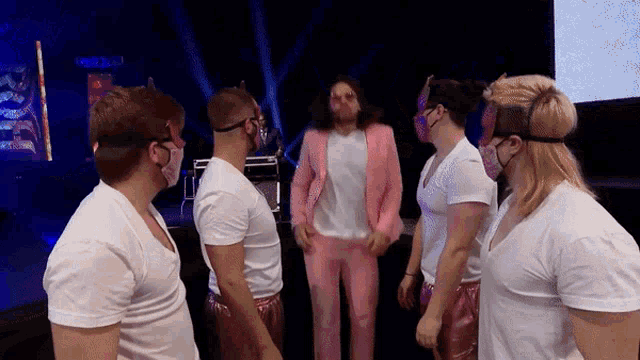 a man in a pink suit is surrounded by a group of men wearing masks