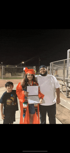 a girl in an orange cap and gown is holding a certificate while standing next to two men