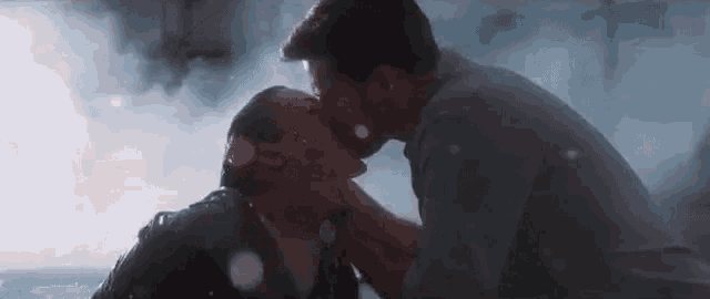 a man and woman are kissing in the rain in a pool .