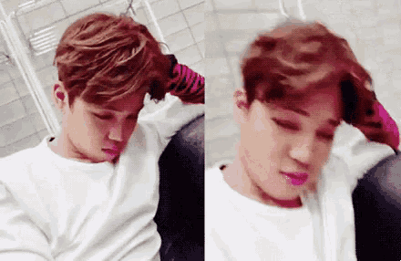 a young man in a white shirt is sitting on a couch and holding his head .