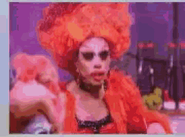 a drag queen wearing an orange wig and a red dress is making a funny face .