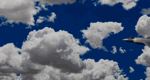a fighter jet flies through a cloudy blue sky