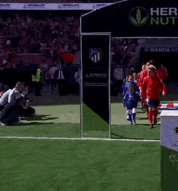 a group of kids are walking on a soccer field in front of a banner that says herbalife