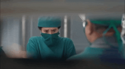 a surgeon with a mask on her face is looking at another surgeon in a hospital room .