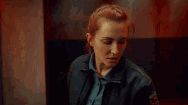 a woman in a blue shirt and black jacket looks up at something