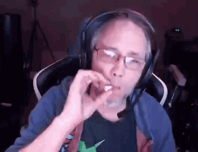 a man wearing headphones and glasses is smoking a cigarette in front of a computer screen .
