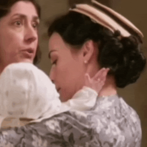 two women are hugging each other in a room and one of them is holding a baby .