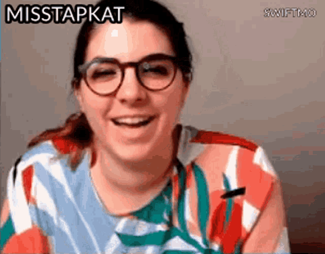 a woman wearing glasses and a colorful shirt is smiling and says misstapkat .
