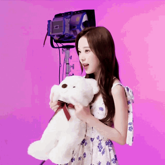 a woman in a floral dress is holding a white teddy bear with a red bow
