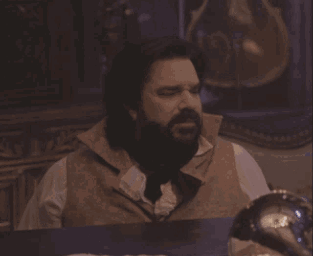a man with a beard sits at a table in front of a mirror