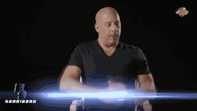 a bald man in a black shirt is sitting in front of a screen that says fast and furious