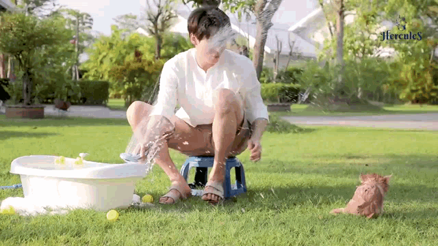 a man is kneeling on a blue stool in the grass with a bucket of water on his head .