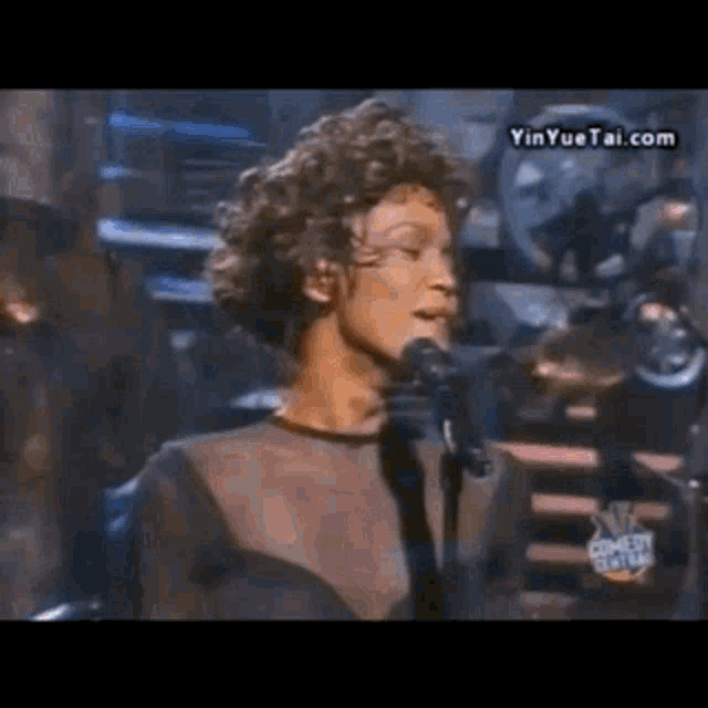 a woman singing into a microphone with the website yinyuetai.com in the background