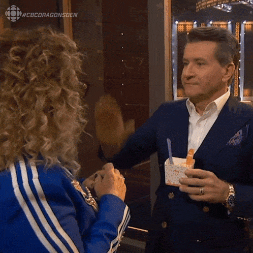 a man in a suit is giving a woman a high five while holding a cup of ice cream