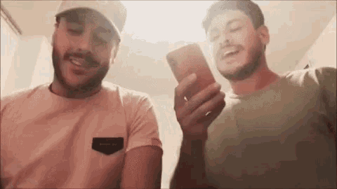 two men are laughing and looking at their phones .