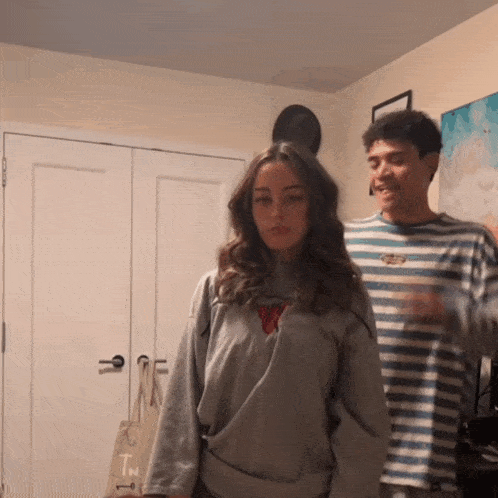 a man in a striped shirt stands next to a woman in a grey sweater
