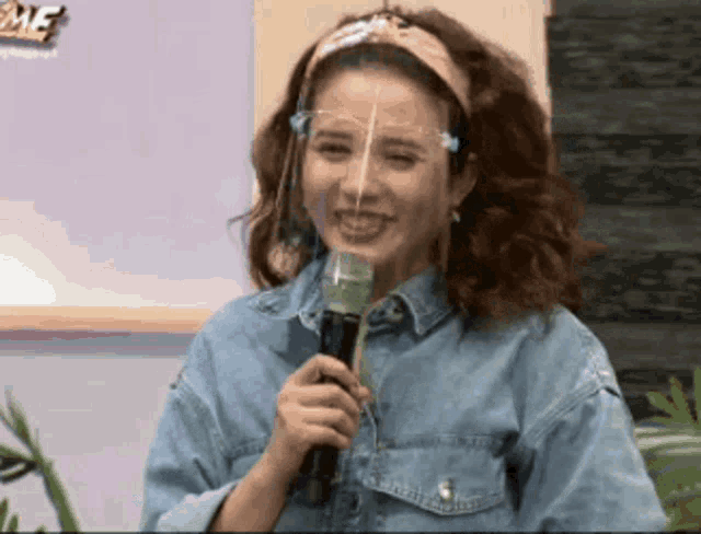 a woman wearing a face shield is holding a microphone .