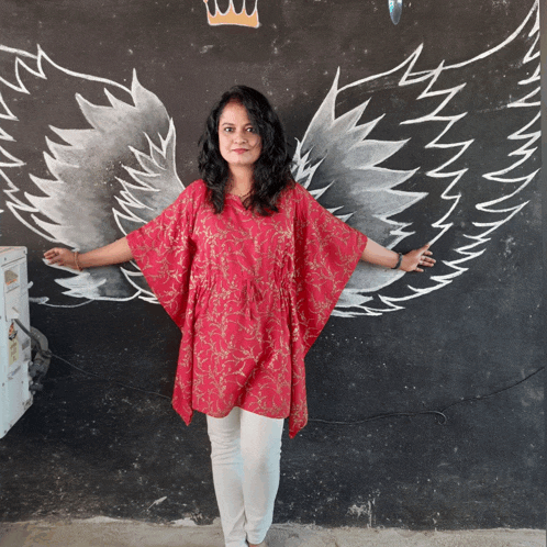 a woman in a red top is standing in front of a black wall with angel wings painted on it