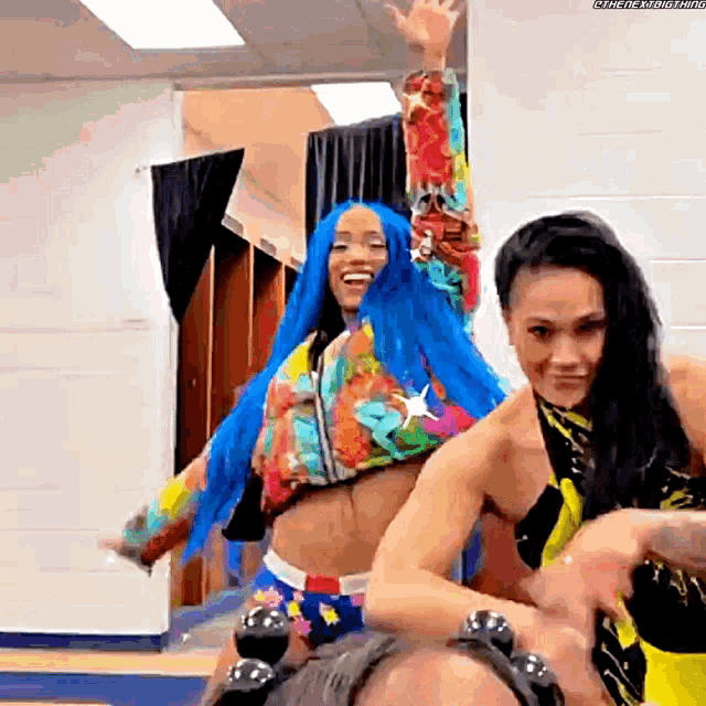 a couple of women are standing next to each other in a room . one of the women has blue hair .