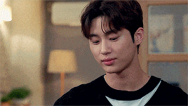 a young man in a black sweater is sitting in a living room looking down .