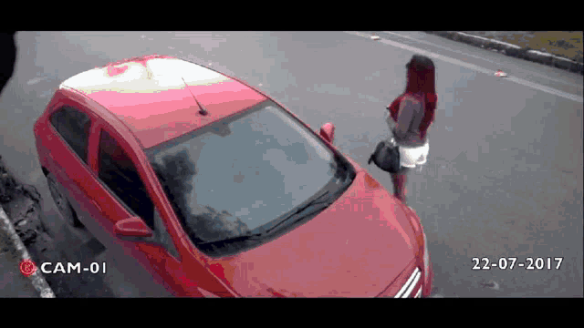 a woman standing next to a red car with cam-01 written on the bottom