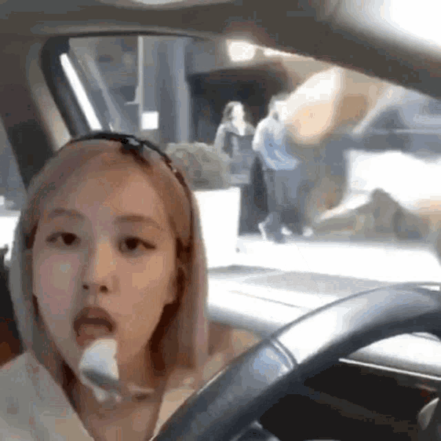 a woman is driving a car with a spoon in her mouth and a man is walking in the background .