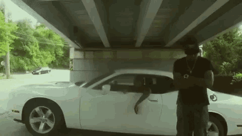 a man is standing next to a white sports car under a bridge .