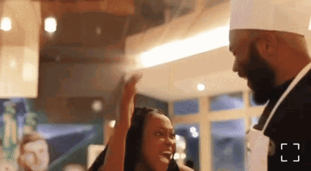 a man in a chef 's hat is talking to a woman in an apron in a restaurant .
