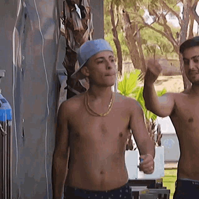 two shirtless men are standing next to each other and one is wearing a hat