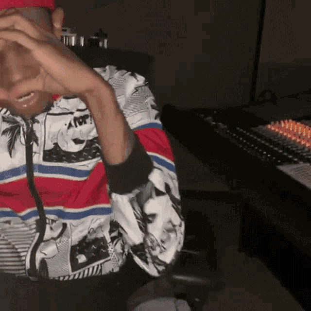 a man wearing a red white and blue striped shirt is sitting in front of a mixing board