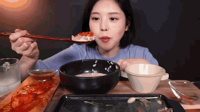 a woman is eating a bowl of food with chopsticks and a spoon .