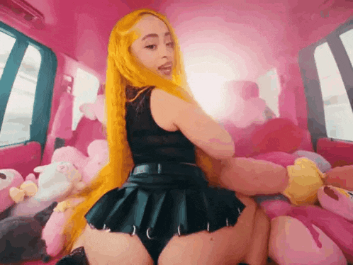 a woman with yellow hair is sitting in a pink car with stuffed animals